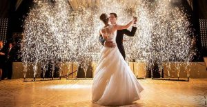 Bride and groom dancing together in an indoor wedding venue surrounded by guests and elegant lighting.